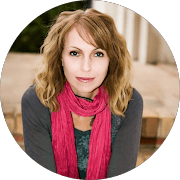 Woman with wavy blonde hair and a bright pink scarf sitting on outdoor brick steps.