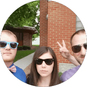 Three people in sunglasses posing outside a brick building, one making a peace sign.